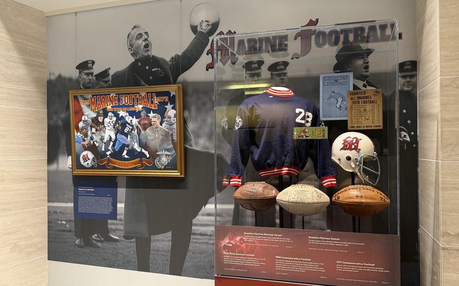 An exhibit featuring a painting, three footballs, and a jersey in a display case.