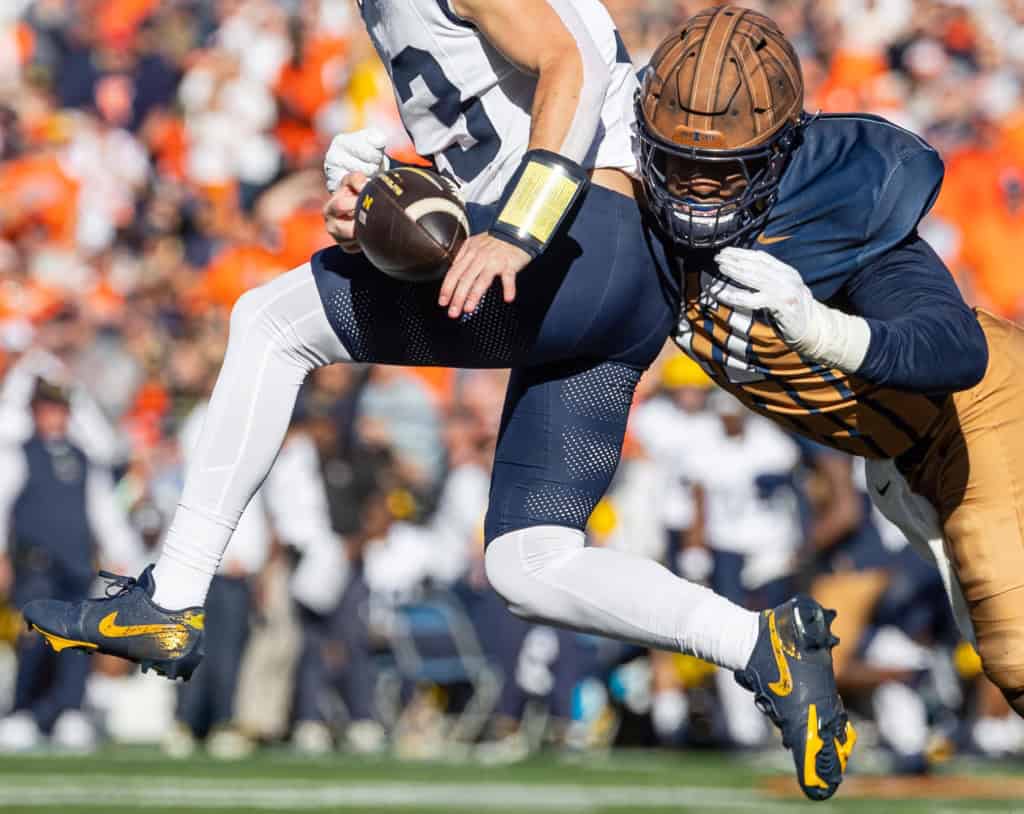 Illinois defensive player, Gabe Jacas, in navy and orange uniform wraps up an opposing quarterback for a sack during live game action.