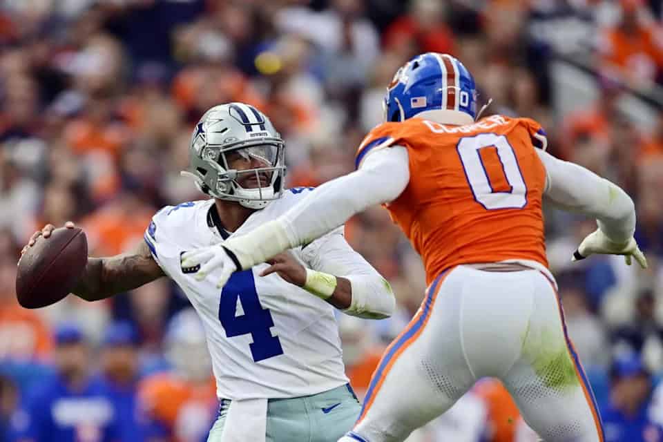 Quarterback Dak Prescott of the Dallas Cowboys throwing a pass during an NFL game against the Denver Broncos with a defender in pursuit.
