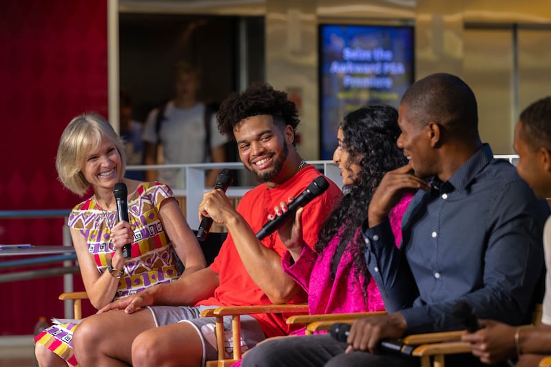 Caleb Williams holds a microphone and smiles while sitting on a panel with USC Annenberg dean Willow Bay and other contributors.