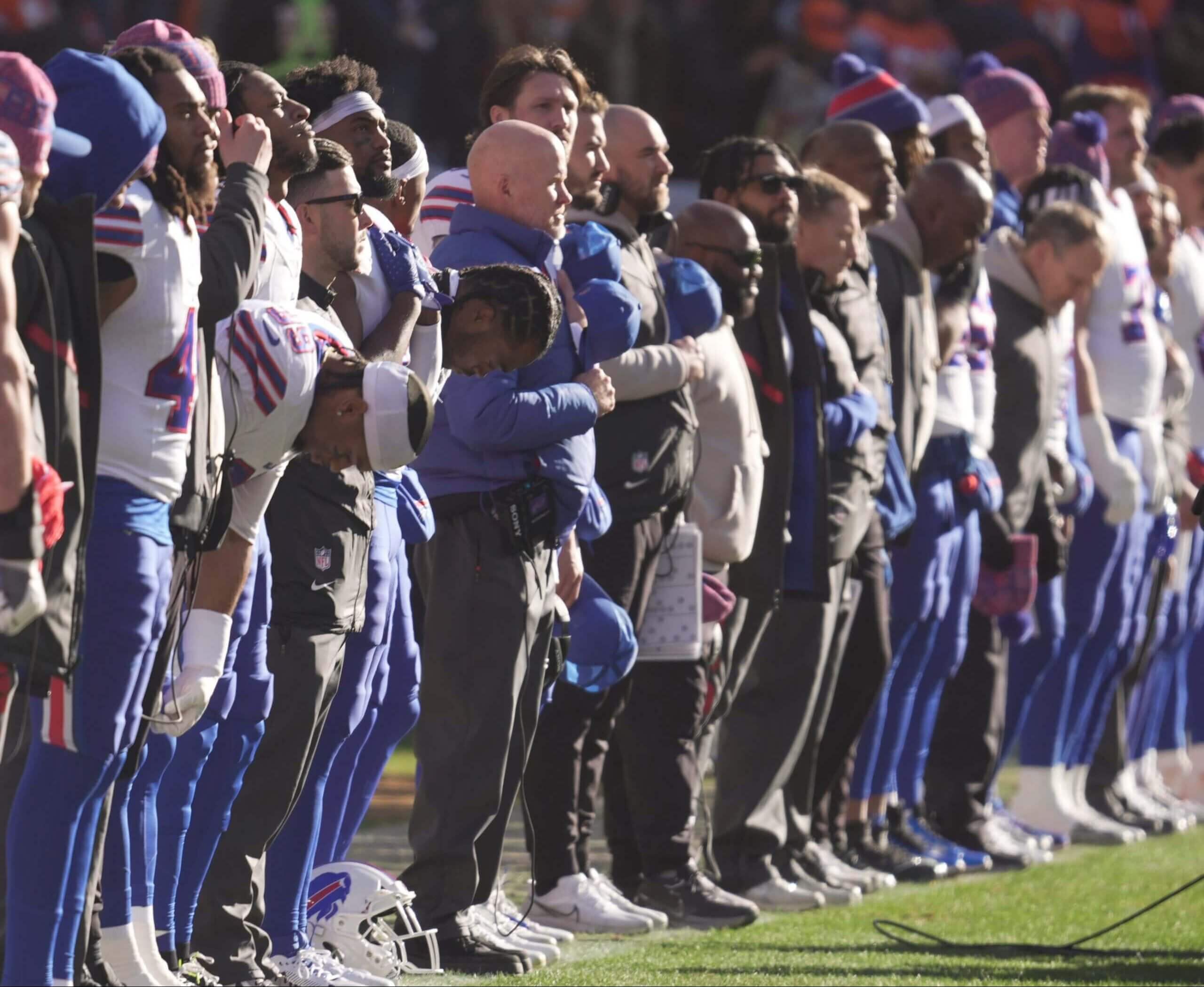 Sean McDermott and his players and fellow coaches stand on the sidelines during the national anthem.