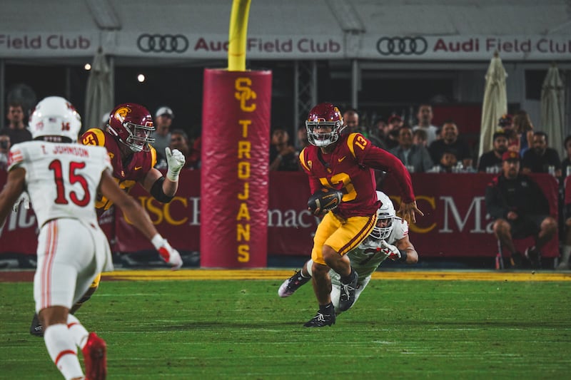 Caleb Williams (13) scrambles to avoid a Utah defender, October 2023. He wears a cardinal and gold USC football uniform.