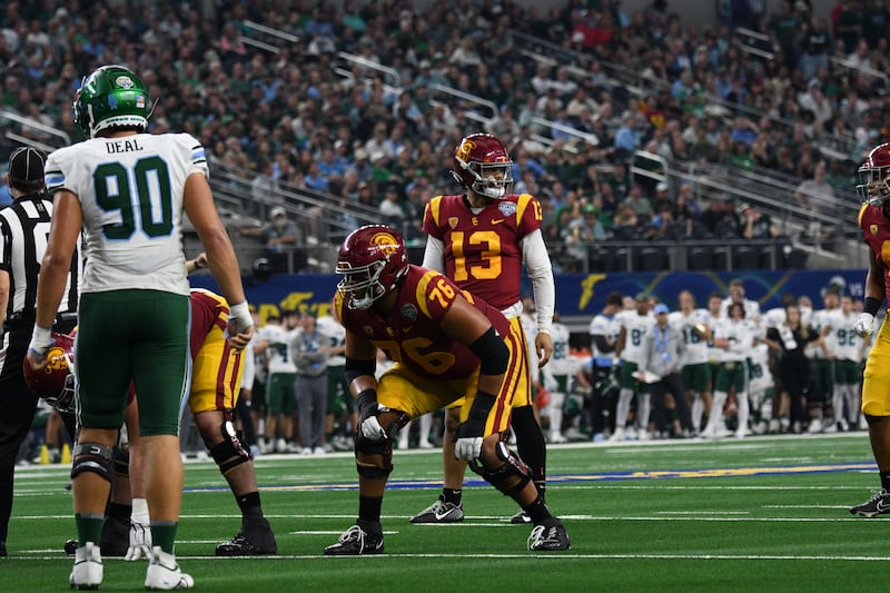 Williams stands behind his linemen before a play; all wear cardinal and gold USC football uniforms.