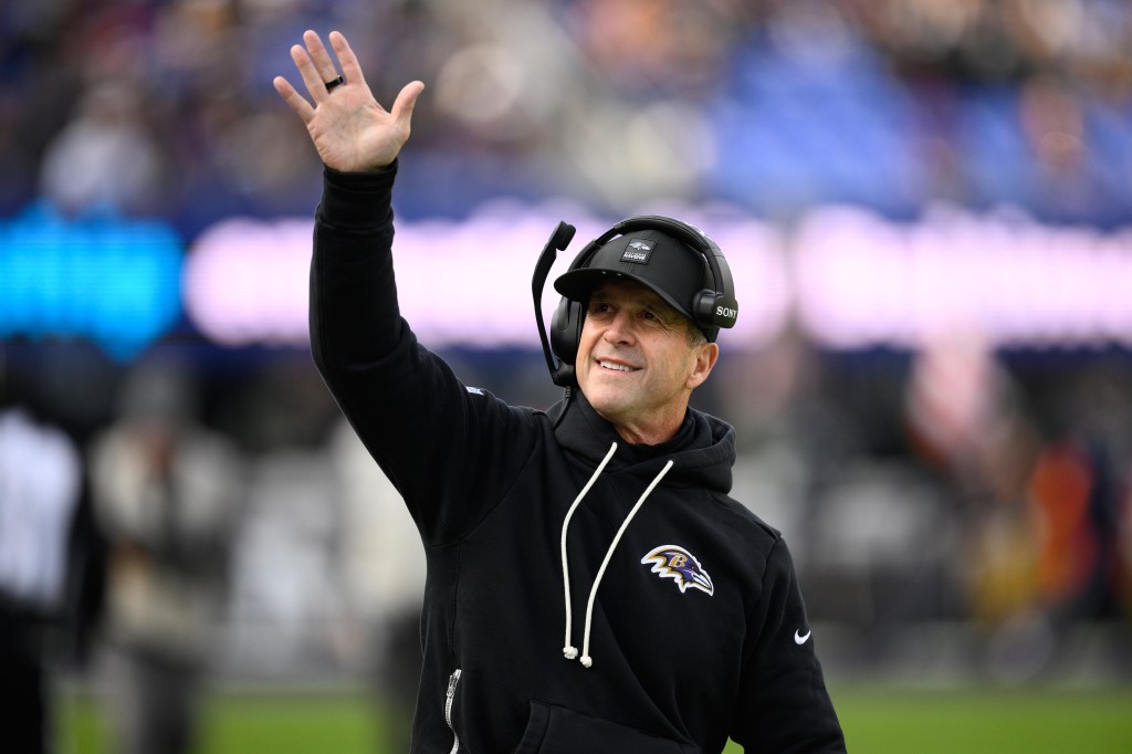 Baltimore Ravens head coach John Harbaugh greets fans at an NFL football game.