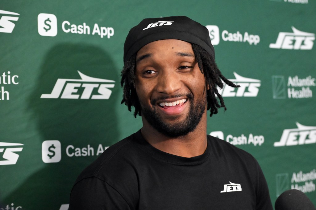 Jets wide receiver Isaiah Williams smiles while wearing a black Jets shirt and cap during a media appearance.