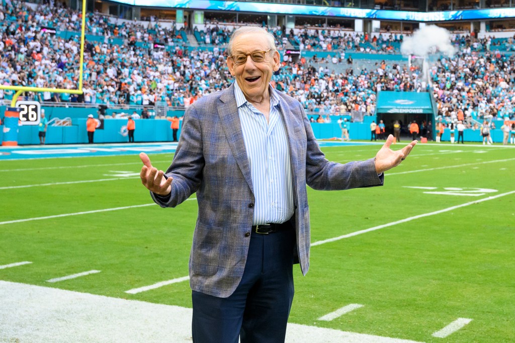 Miami Dolphins owner Stephen Ross gestures and smiles on the football field during a game.