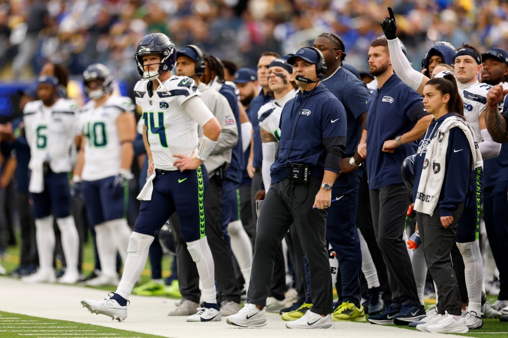 Sam Darnold and Coach Mike Macdonald of the Seattle Seahawks watch the game from the sidelines.