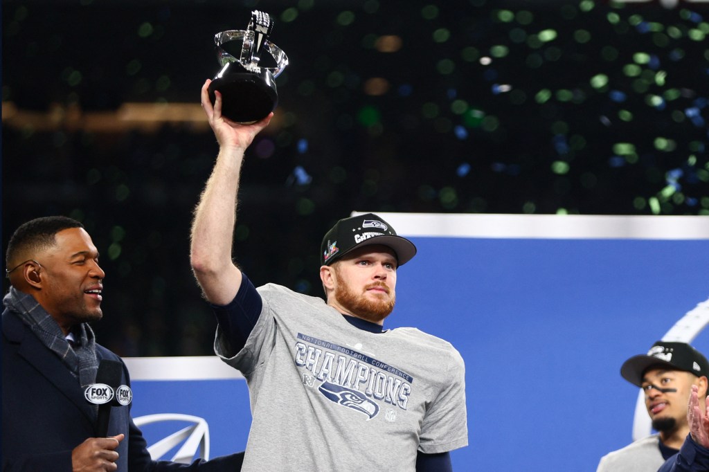 Seattle Seahawks quarterback Sam Darnold holding the NFC Championship trophy with confetti falling.