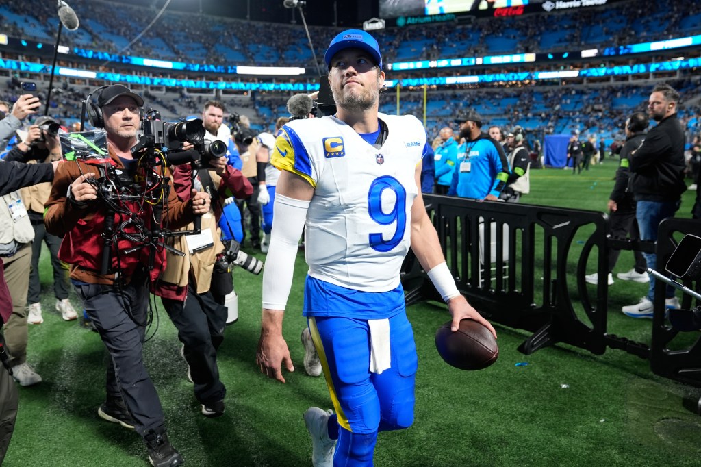 Los Angeles Rams quarterback Matthew Stafford walks off the field after a win, holding a football.