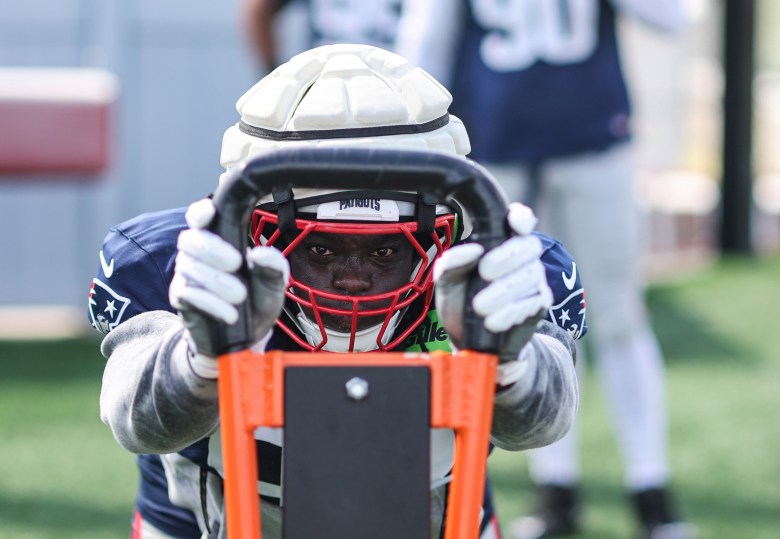 New England Patriots defensive lineman Jeremiah Pharms moves laterally during a practice drill on the field, wearing a navy practice jersey and protective helmet.