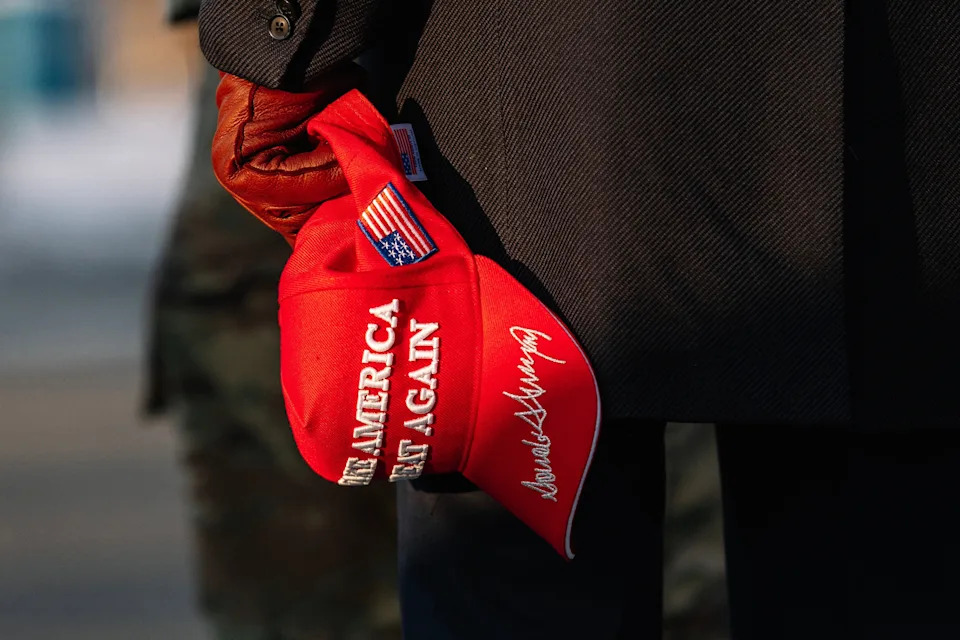 Person holding a red cap with a slogan, featuring a notable signature, while standing outdoors