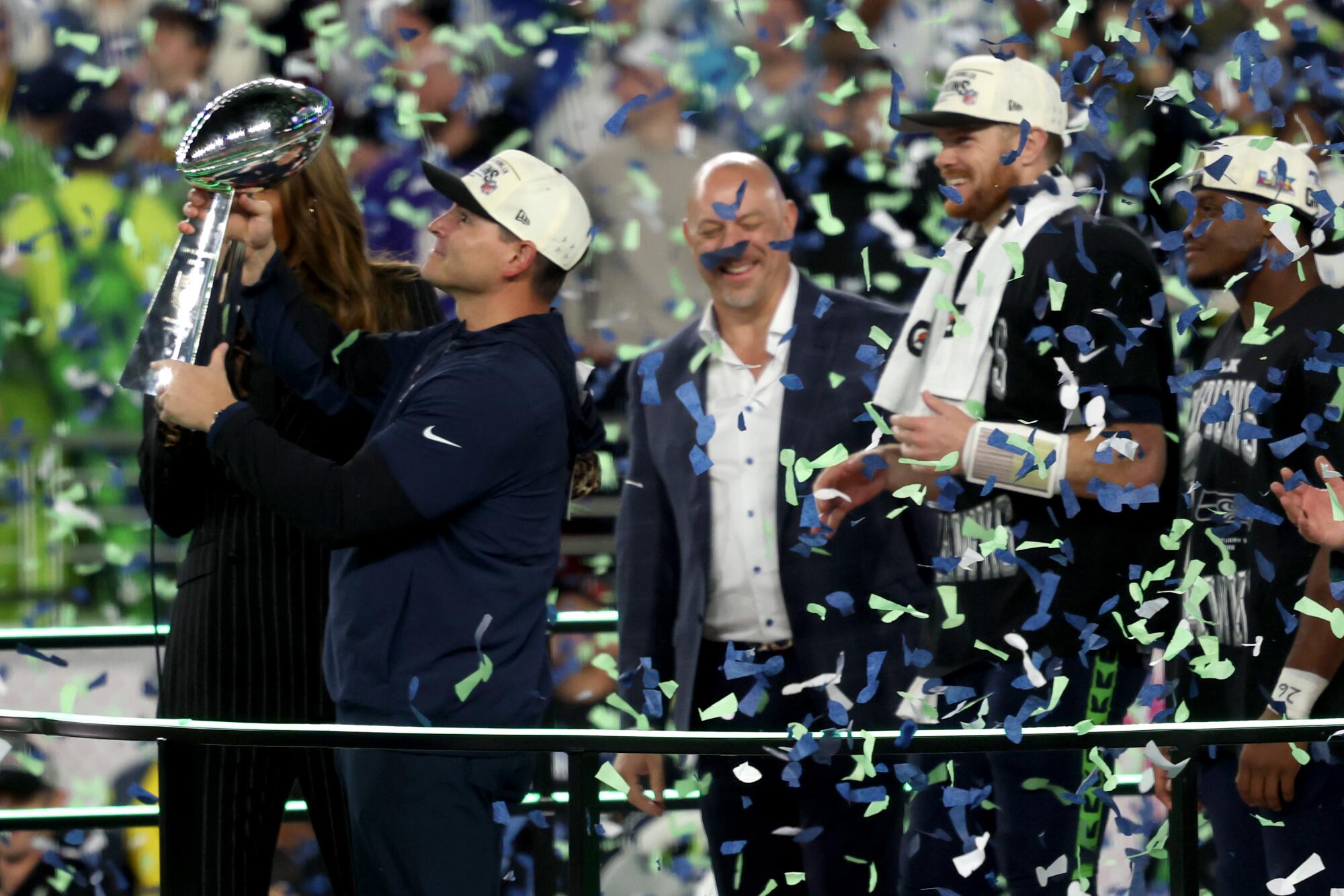 Seahawks coach Mike MacDonald holds the Vince Lombardi Trophy on stage in front of Sam Darnold and Kenneth Walker III.