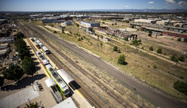 A group of people in hard hats fling shovels toward the sky as dirt rains down around them.
