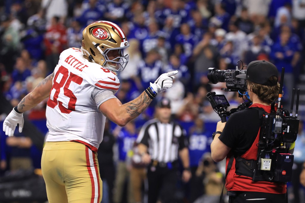 San Francisco 49ers player George Kittle wearing number 85, pointing, while a cameraman films him.