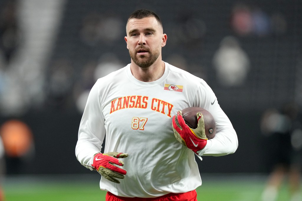 Travis Kelce holding a football, wearing a white Kansas City Chiefs long-sleeved shirt with the number 87.