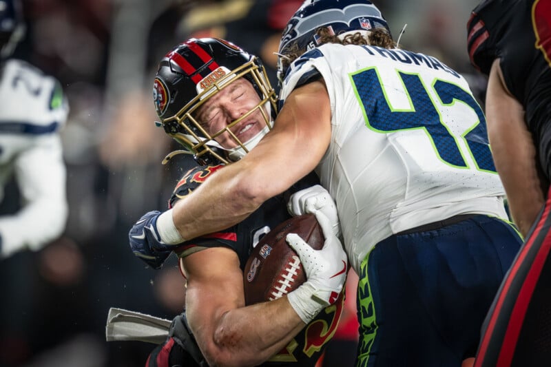 A Seattle Seahawks player tackles a San Francisco 49ers player holding the football tightly during an intense NFL game, with both athletes showing determination and physical effort.