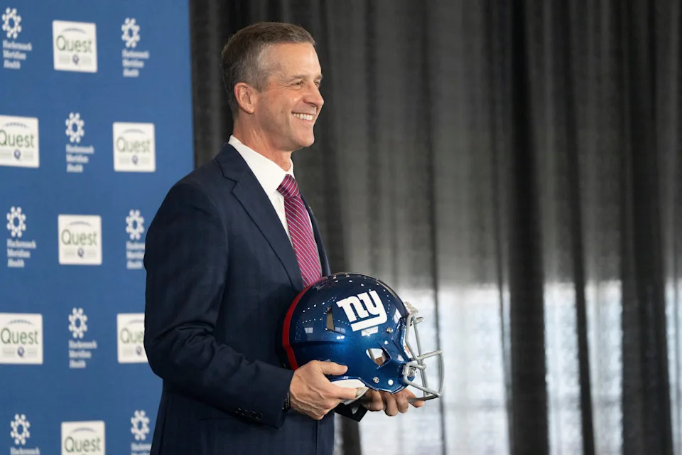 New Giants head coach John Harbaugh holds up a helmet.
