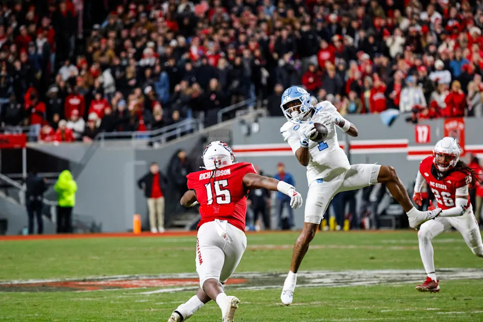 Nov 29, 2025; Raleigh, North Carolina, USA; North Carolina Tar Heels cornerback Thaddeus Dixon (1) catches the football in the air over NC State Wolfpack linebacker AJ Richardson (15) during the first half of the game at Carter-Finley Stadium. Mandatory Credit: Jaylynn Nash-Imagn Images