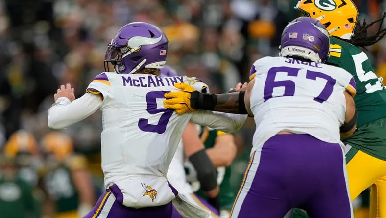 J.J. McCarthy is pressured by Packers defenders during a Vikings game at Lambeau Field.