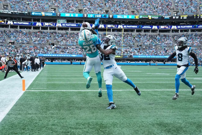 Oct 5, 2025; Charlotte, North Carolina, USA; Miami Dolphins running back De'Von Achane (28) catches a touchdown pass as Carolina Panthers linebacker Trevin Wallace (32) defends in the second quarter at Bank of America Stadium. Mandatory Credit: Bob Donnan-Imagn Images