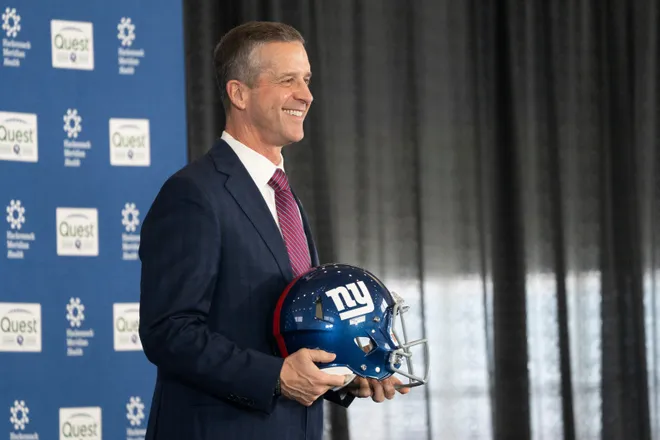 New Giants head coach John Harbaugh holds up a helmet.