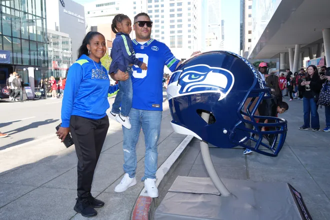 Seattle Seahawks fans pose with a large helmet at the Super Bowl LX Experience.