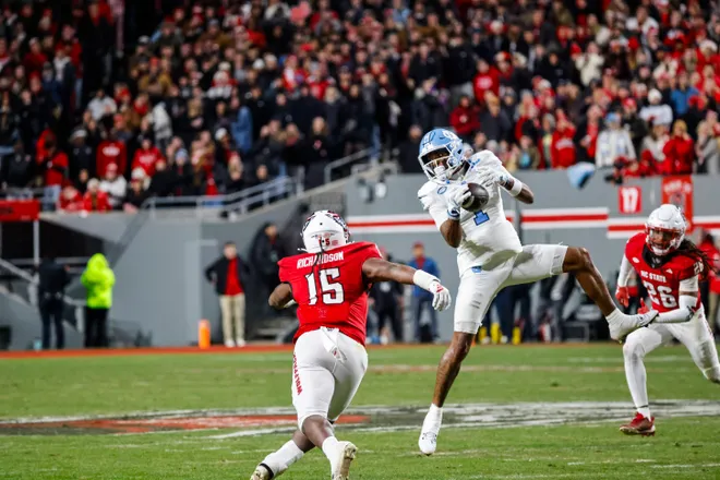 Nov 29, 2025; Raleigh, North Carolina, USA; North Carolina Tar Heels cornerback Thaddeus Dixon (1) catches the football in the air over NC State Wolfpack linebacker AJ Richardson (15) during the first half of the game at Carter-Finley Stadium. Mandatory Credit: Jaylynn Nash-Imagn Images
