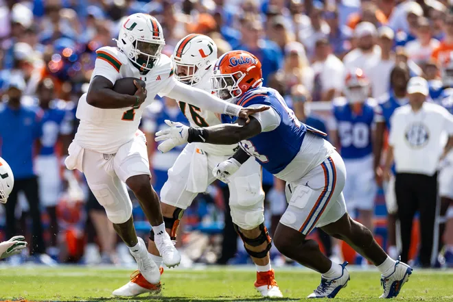 Aug 31, 2024; Gainesville, Florida, USA; Miami Hurricanes quarterback Cam Ward (1) runs past Florida Gators defensive lineman Caleb Banks (88) during the first half at Ben Hill Griffin Stadium. Mandatory Credit: Matt Pendleton-USA TODAY Sports