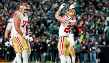 Two San Francisco 49ers players celebrate in the end zone during a night football game with a crowd in the background.