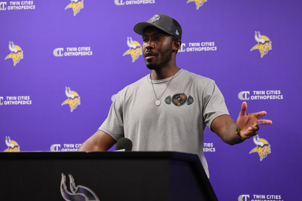 Kwesi Adofo-Mensah speaking at a press conference with Twin Cities Orthopedics and Minnesota Vikings logos on a purple background.