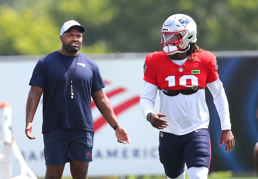Patriots quarterback Drake Maye in a red jersey and helmet with a coach.