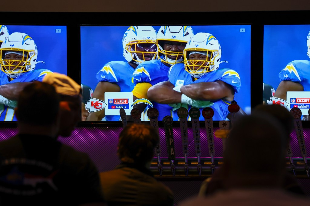 Two men watching an NFL game telecast on YouTube TV on multiple screens in a bar.