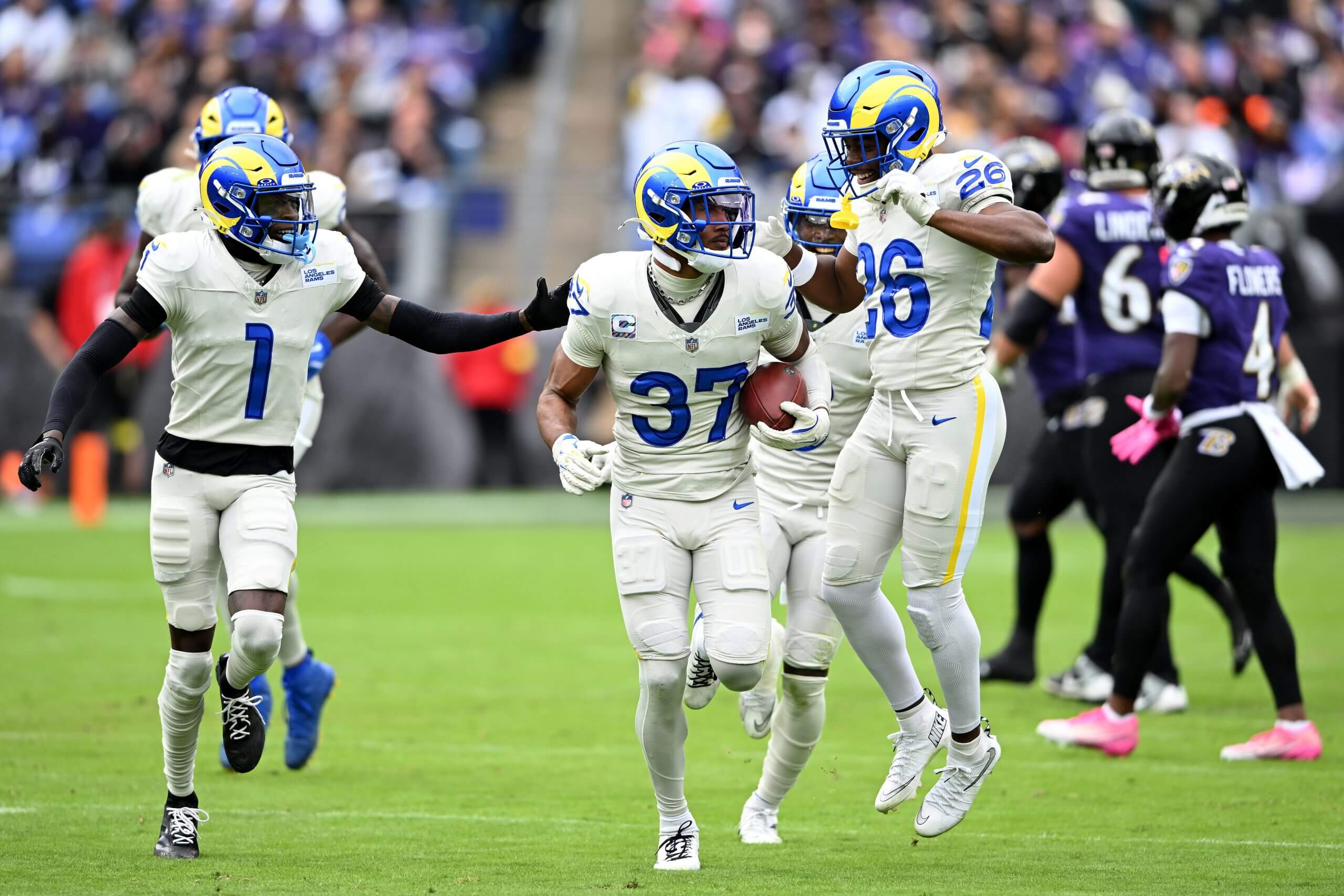 Quentin Lake of the Rams, with teammates around him, carries a football in his left arm.