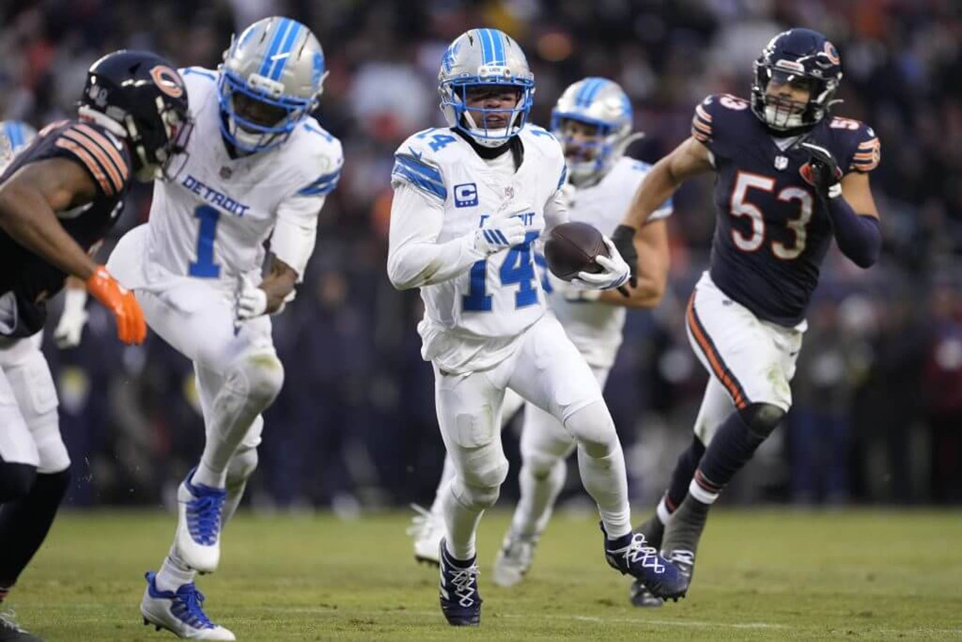 An image of Detroit Lions wide receiver Amon-Ra St. Brown running with the football in his left hand while Chicago Bears players pursue him during an NFL game.