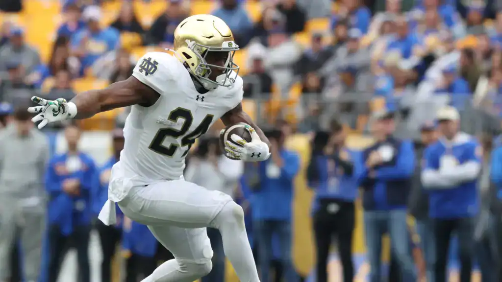 Jadarian Price accelerates upfield with the ball in a Notre Dame road uniform, showing burst and balance.