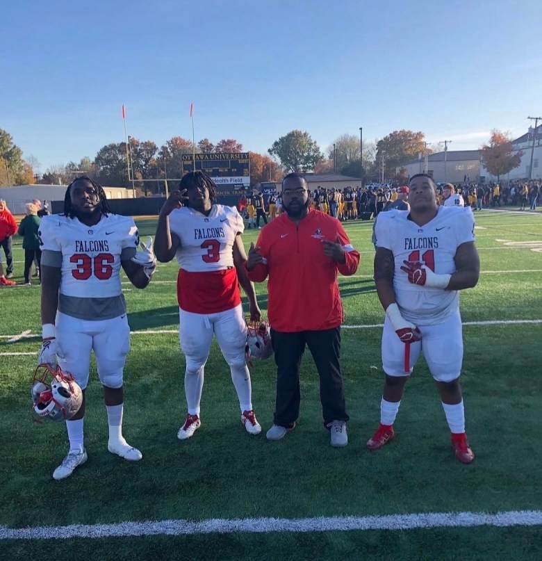 Jeremiah Pharms stands on a football field with teammates and his trainer, James Tabor, after a game.