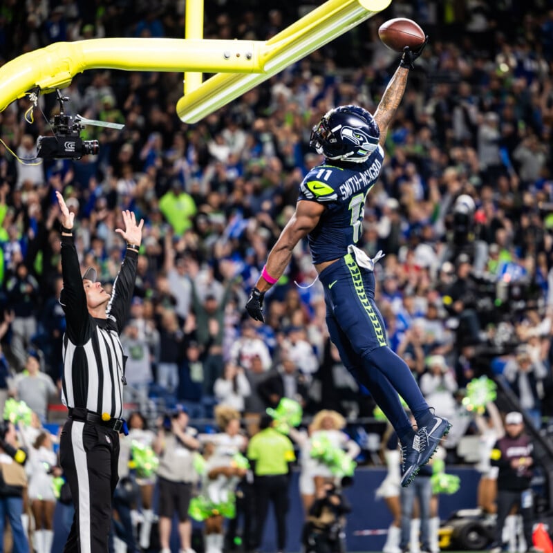 A Seattle Seahawks player leaps and dunks a football over the goalpost while a referee raises both arms, with a cheering crowd in the background.