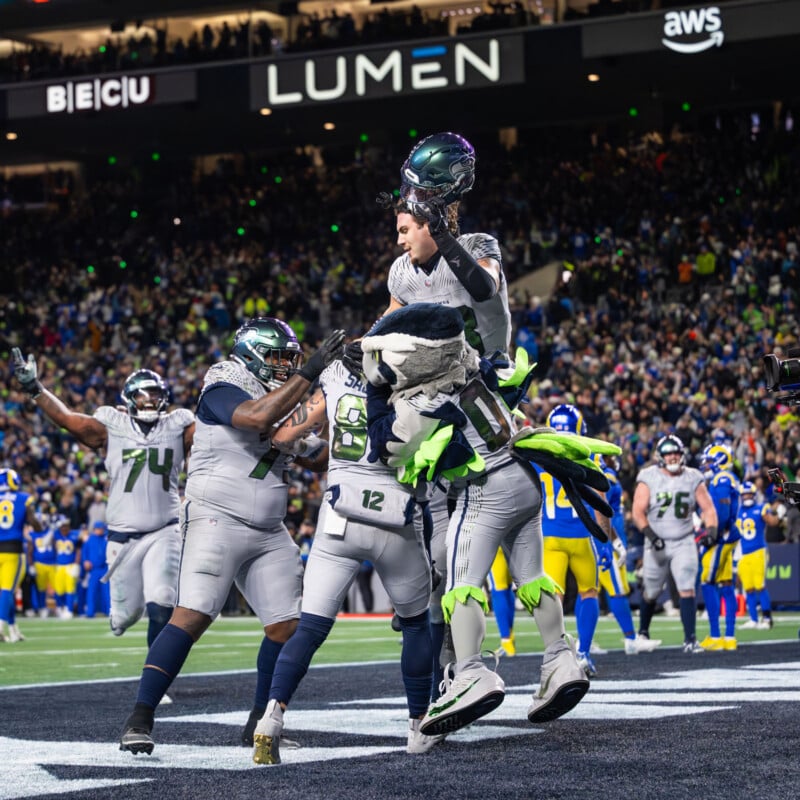 Seattle Seahawks players and their mascot celebrate in the end zone during a football game, with a crowd of fans and stadium lights in the background.