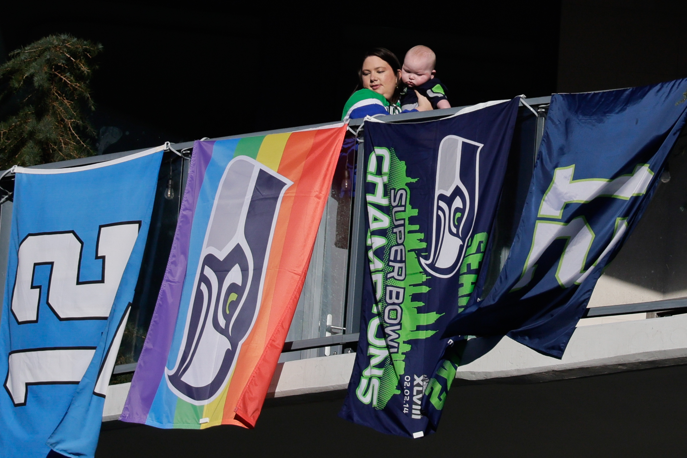 A person holds a baby with Seahawks flags below them.