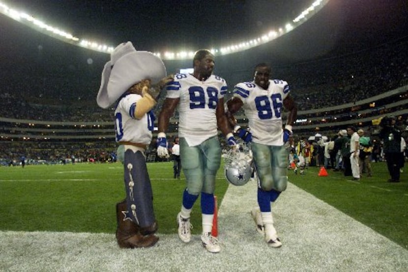 Cowboys Greg Ellis (98) and Mike Lucky (86) are congratulated by mascot Rowdy as they walk...