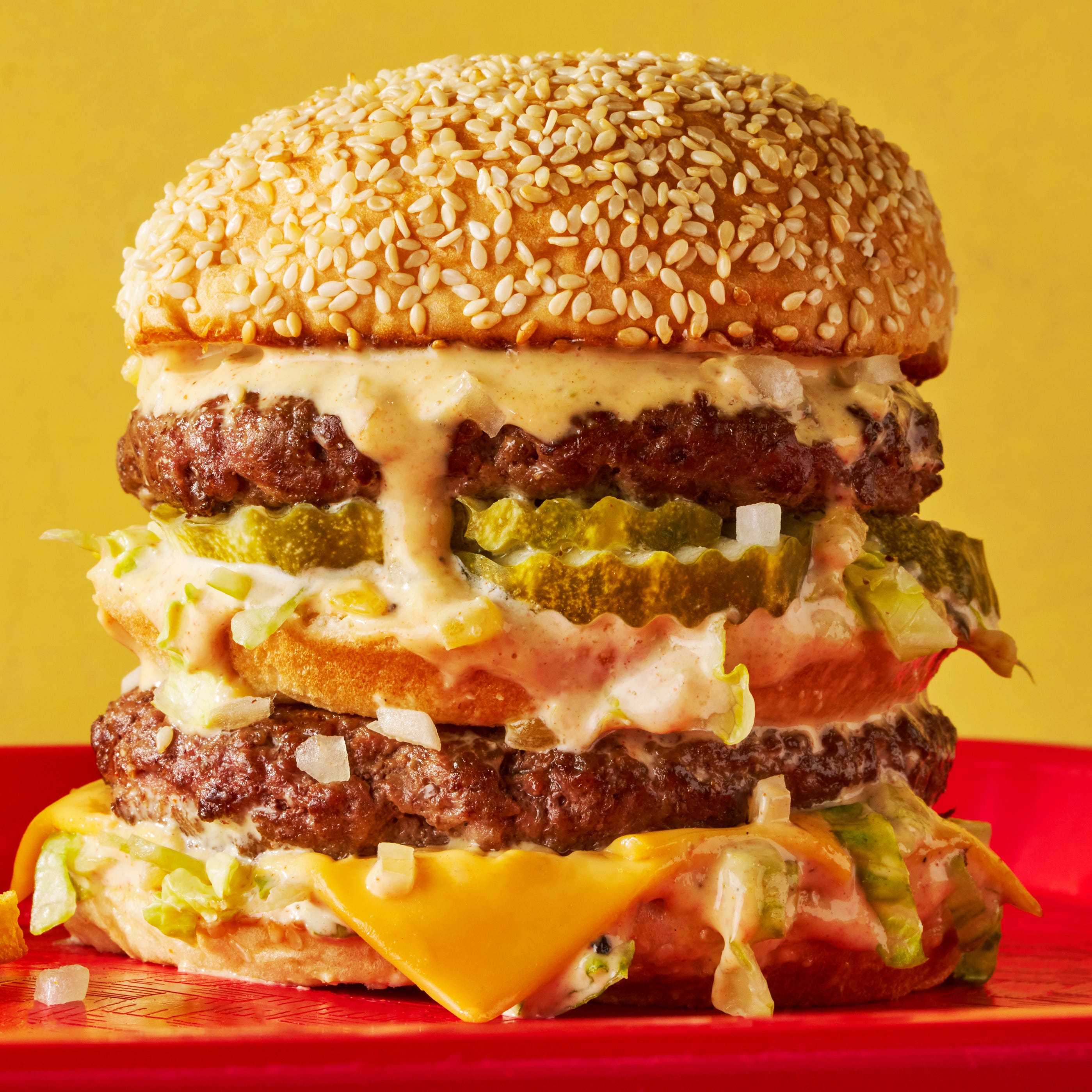 two patties stacked between three buns with melted cheese, lettuce, onions, and special sauce