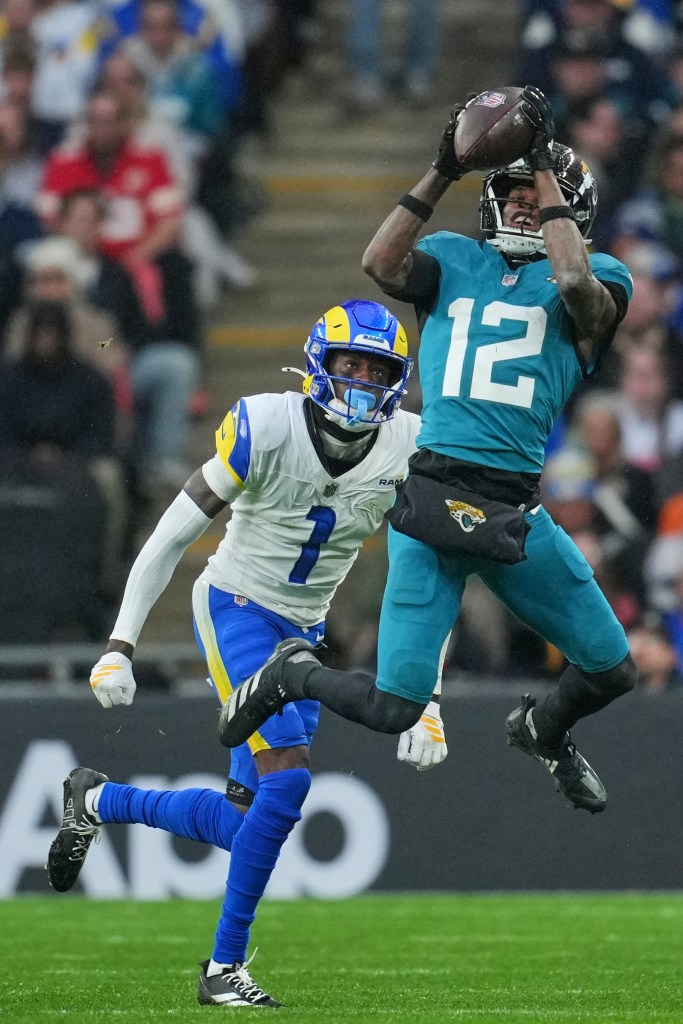 Jacksonville Jaguars wide receiver Travis Hunter (12) catching a football while Los Angeles Rams defender Emmanuel Forbes Jr. closes in.