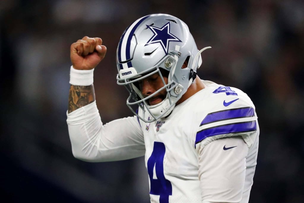 Cowboys football player, Dak Prescott, whose contract restructure could fix the Cowboys cap space, in a Dallas Cowboys uniform celebrating victory on the field, wearing helmet, with arm raised in triumph, during an NFL game.