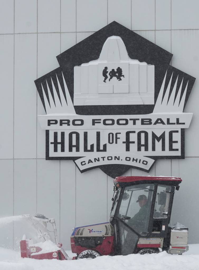 A man in a snowplow clears snow in front of the Pro Football Hall of Fame sign in Canton, Ohio.