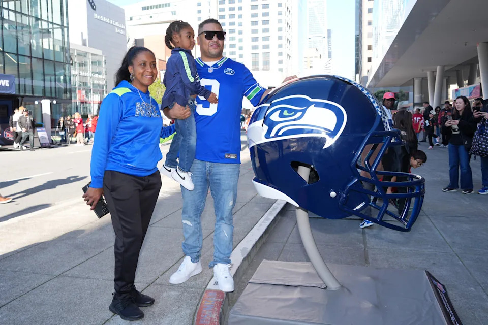 Seattle Seahawks fans pose with a large helmet at the Super Bowl LX Experience.