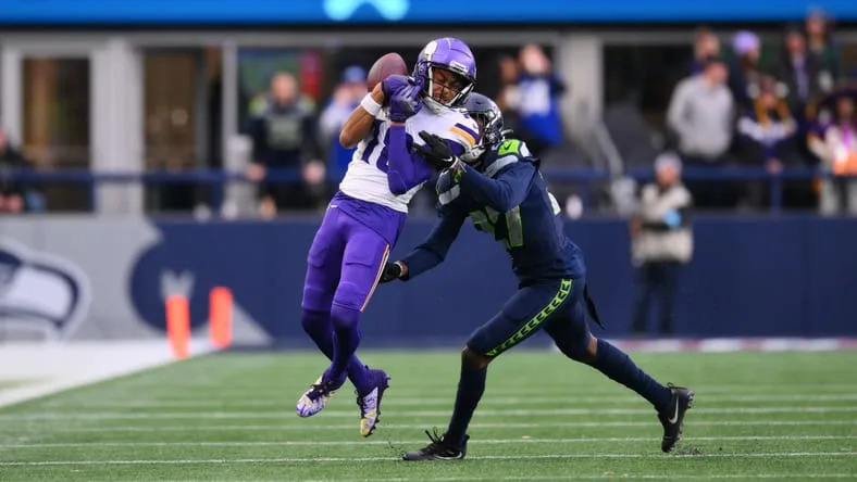 Dec 22, 2024; Seattle, Washington, USA; Minnesota Vikings wide receiver Justin Jefferson (18) catches a pass while defended by Seattle Seahawks cornerback Riq Woolen (27) during the second half at Lumen Field. Mandatory Credit: Steven Bisig-Imagn Images.