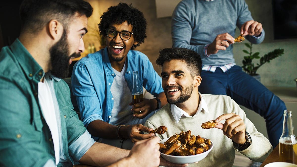 Male friends eating wings, watching spots and drinking beer.