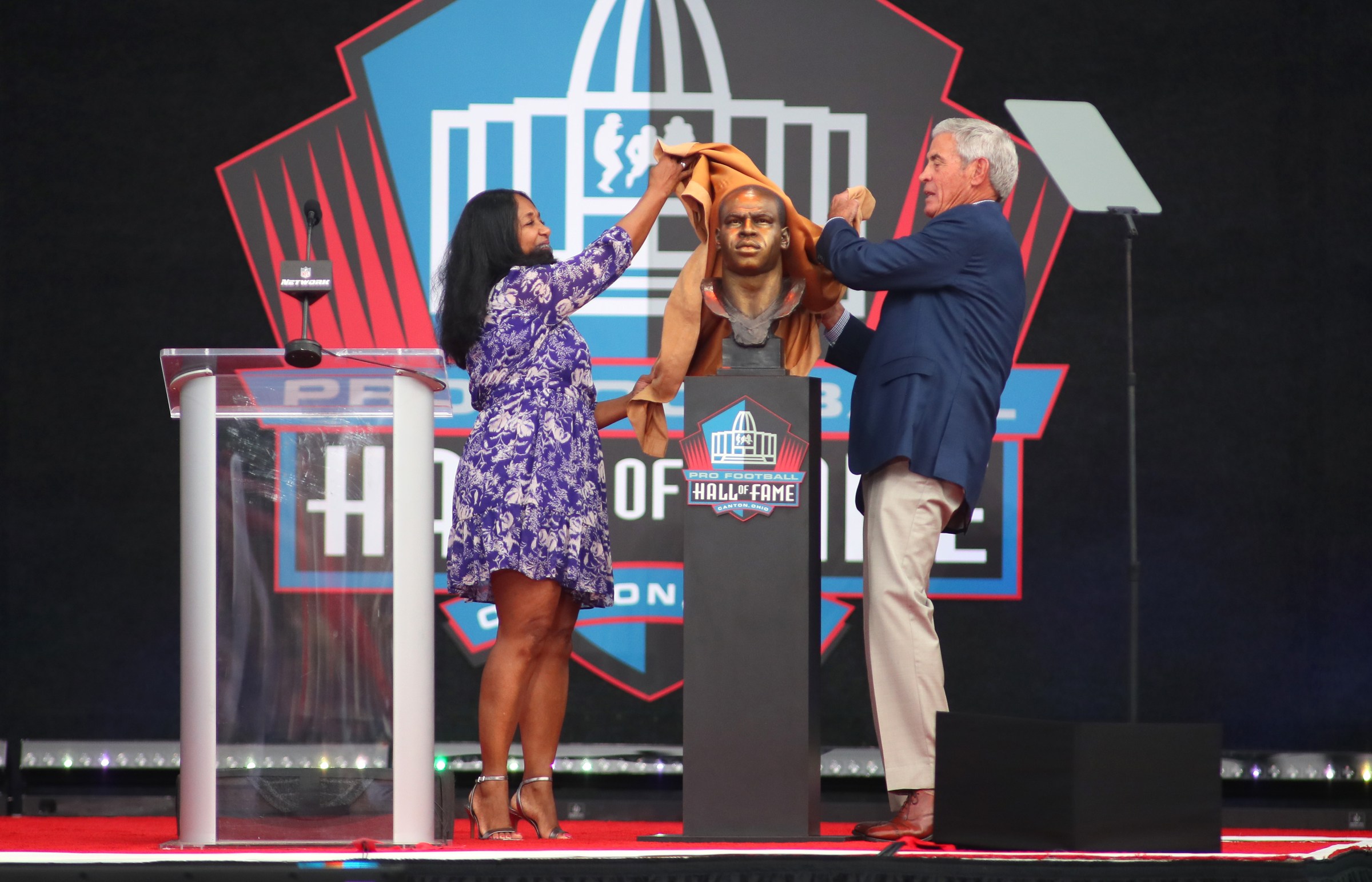 CANTON, OH - AUGUST 06: Sam Mills’ widow, Melanie Mills (left) unveils her husbands bust with his former head coach Jim Mora (right) after his induction into the Pro Football Hall of Fame on August 6, 2022 at Tom Benson Stadium in Canton, Ohio. (Photo by Michael Longo/Icon Sportswire via Getty Images)