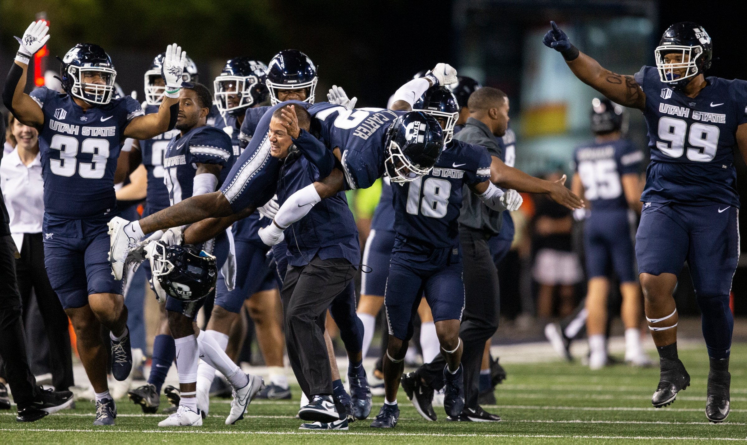 Defensive Coordinator Ephraim Banda carries Ajani Carter #12 of the Utah State Aggies after he intercepted a pass in the endzone
