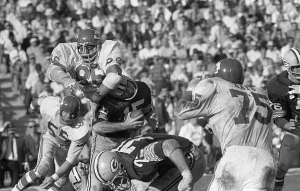Green Bay Packers' quarterback Bart Starr (holding ball) has a bad moment on the field during the Super Bowl despite leading his team to a 35-10 win over the Kansas City Chiefs.  Smothering Starr for a 7 yard loss in the third quarter are the Chiefs' Ed Holub (55) and Buck Buchanan (86).  Green Bay's Forrest Gregg (75) goes down in front of Starr.  (Photo by Bettmann Archive/Getty Images)